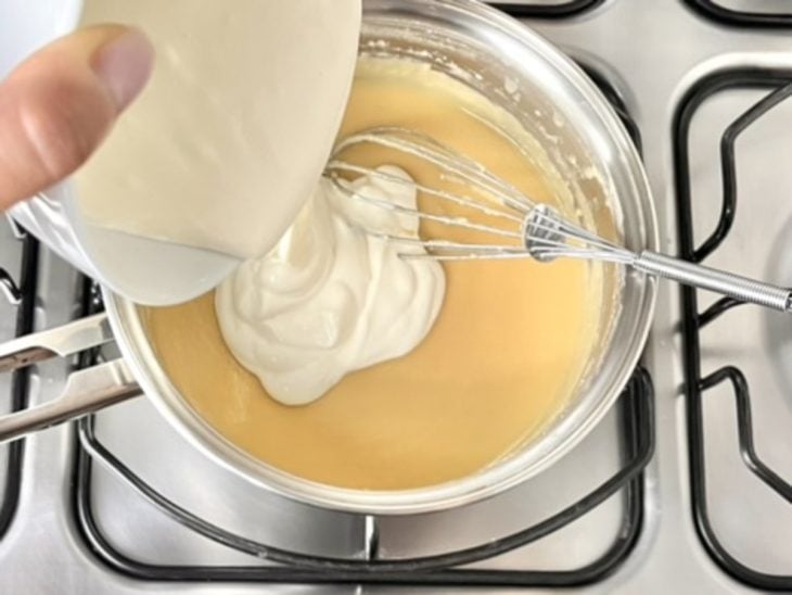 Uma panela com a mistura de leite condensado, manteiga, suco de laranja, sal e creme de leite.