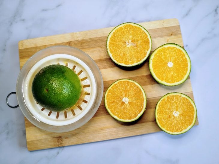 Uma tábua com laranjas cortadas e um espremedor.