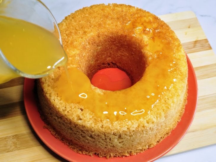 Um bolo e jarra com calda de laranja para bolo.
