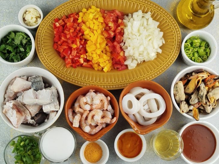 Ingredientes organizados na bancada com frutos do mar e legumes picados.