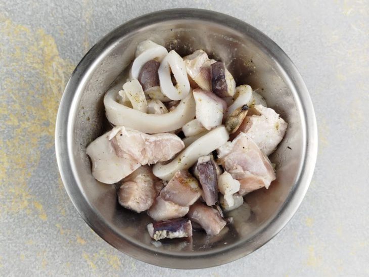 Peixe e lula sendo cortados e temperados com limão, sal e pimenta.