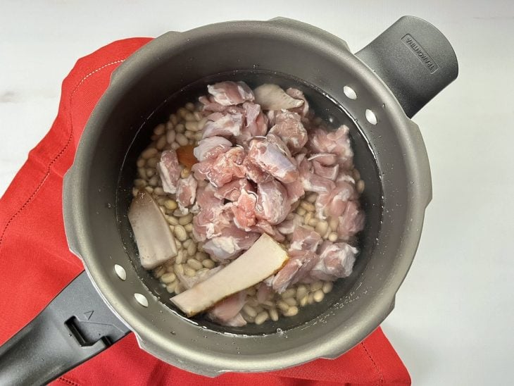 Uma panela de pressão com feijão, as carnes e água.