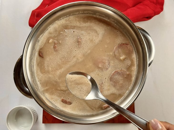 Uma panela com caldo de feijão e uma colher para remover a espuma.