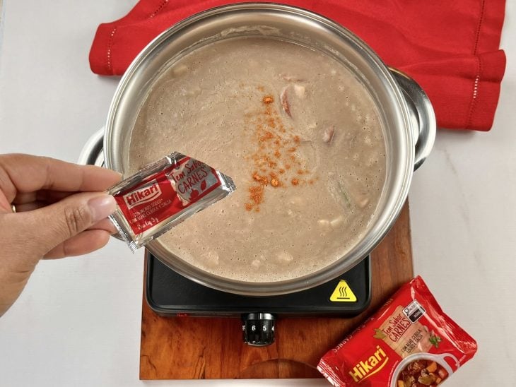 Uma panela com caldo de feijão cozinhando e a adição de tempero.