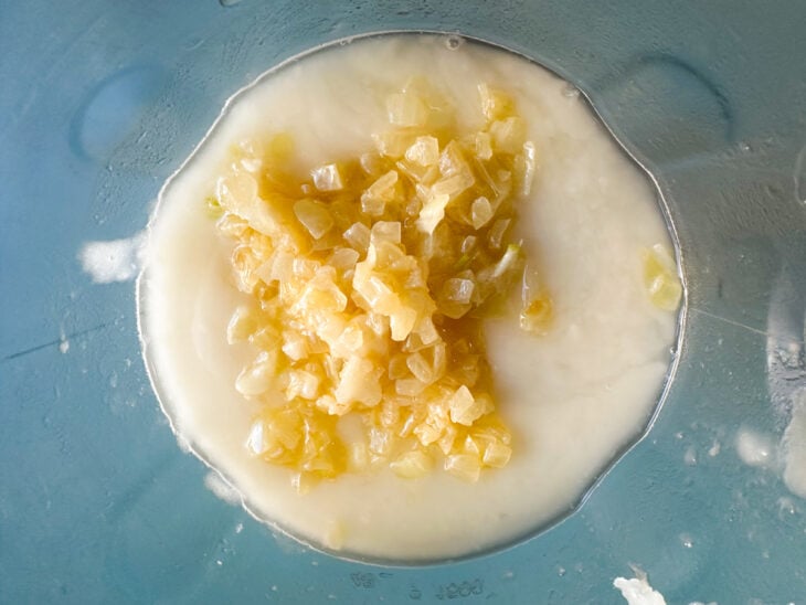 Parte da cebola refogada sendo adicionada ao liquidificador para ser triturada junto ao creme de aipim.