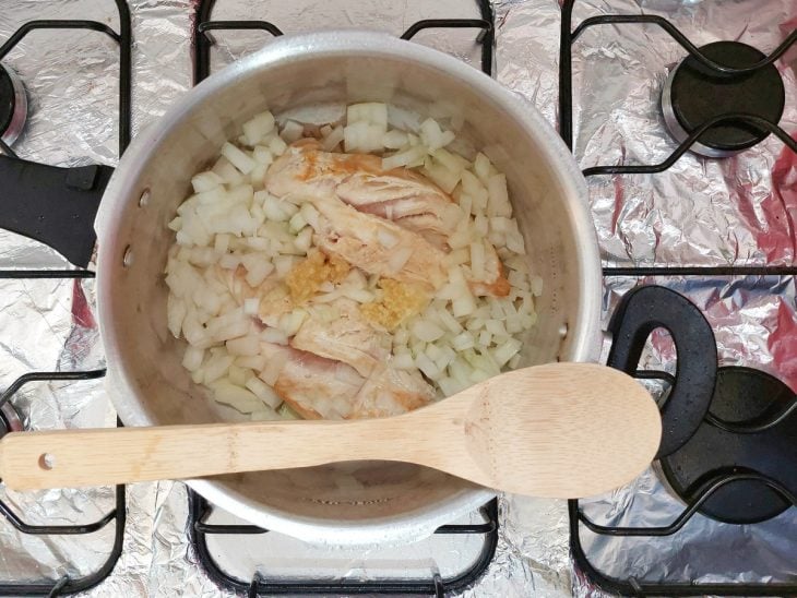 Uma panela de pressão refogando o frango, alho e cebola.