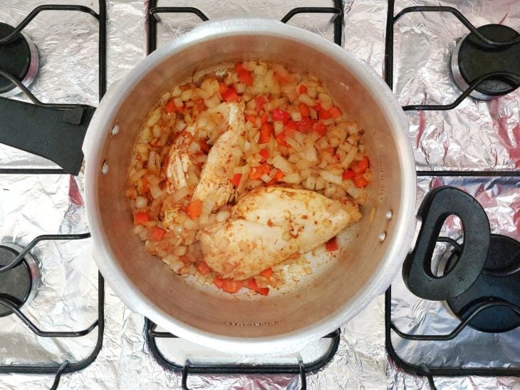 Uma panela de pressão refogando o frango, alho, cebola, pimentão e temperos.