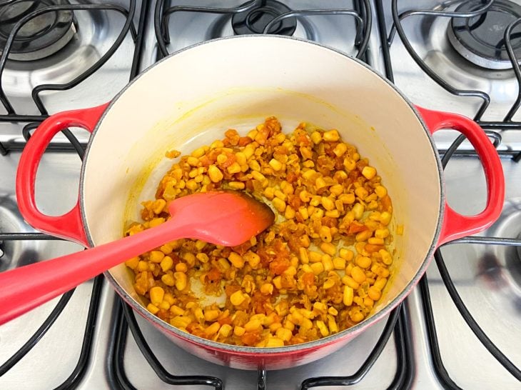 Uma panela com cebola, tomate, sal, pimenta-do-reino, açafrão e milho.