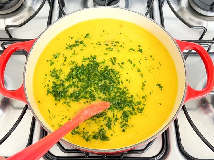 Uma panela com o frango temperado e o caldo de mandioca, com a adição de salsinha.