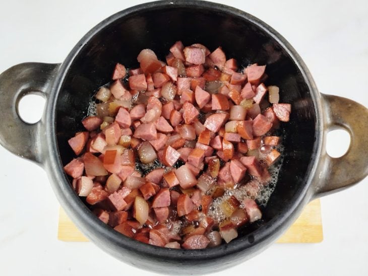Uma panela com calabresa e bacon a dourar.