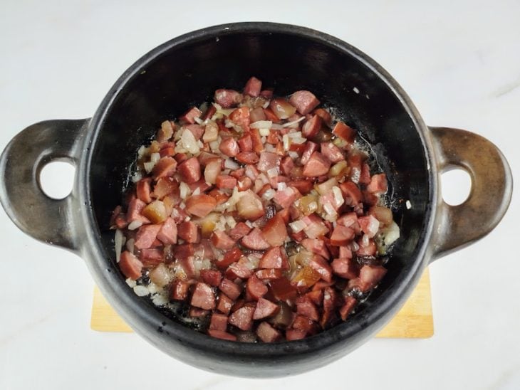 Uma panela com calabresa, bacon, alho e cebola a dourar.