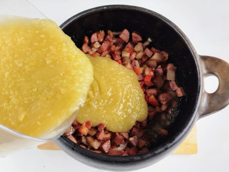 Mandioca batida sendo adicionada à panela com o restante dos ingredientes.