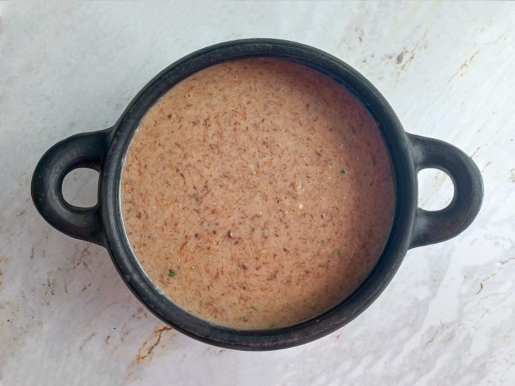 Caldo de mandioca batido, carne desfiada, manteiga, cheiro-verde e sal misturados em uma panela.
