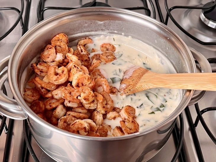 Uma panela contendo creme branco, espinafre e os camarões fritos.