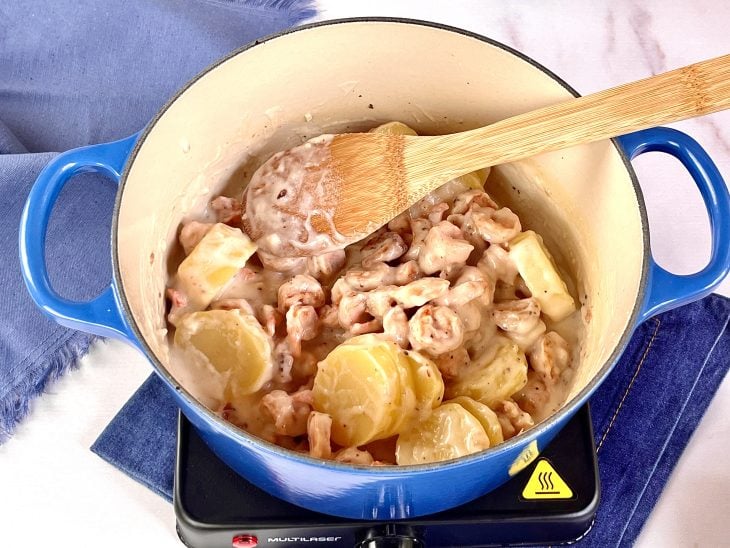 Panela com camarão, molho branco e batatas sendo misturados.