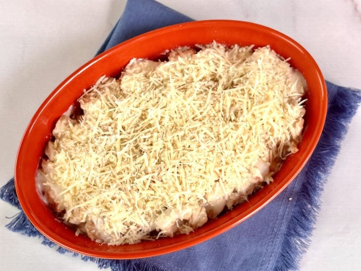 Queijo ralado por cima do camarão ao molho branco no refratário.