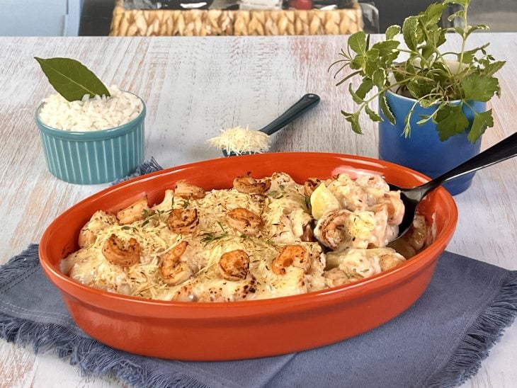 Camarão ao molho branco gratinado com batata em um refratário com uma porção sendo servida.