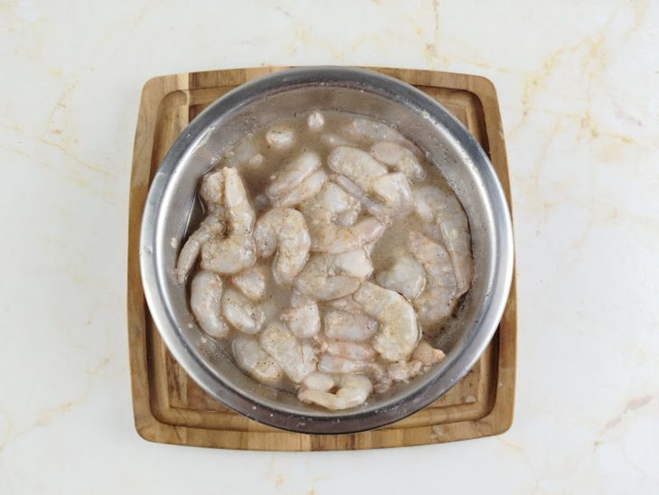 Numa tigela, os camarões temperados com o suco de limão, o alho picado, o sal e a pimenta-do-reino.