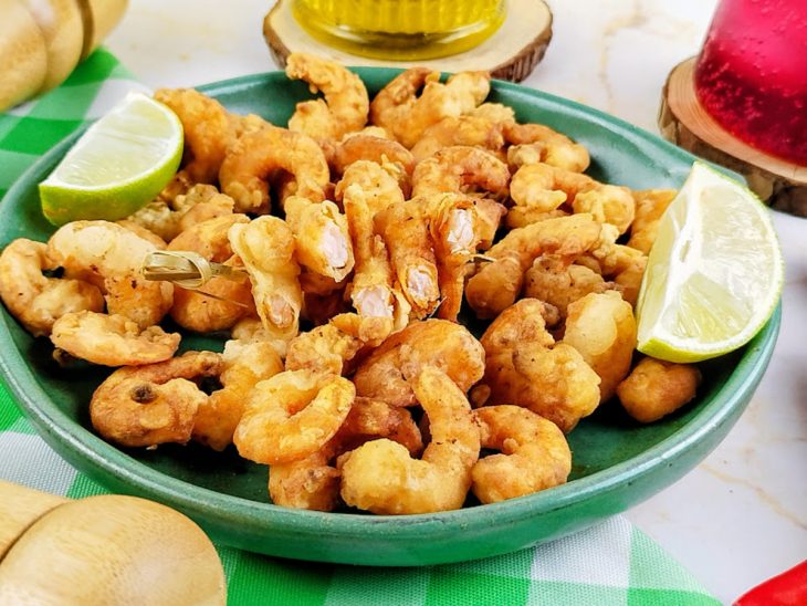 Camarões prontos, servidos em prato fundo, com limões.