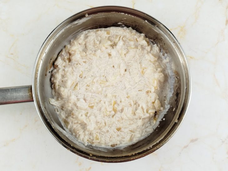 Arroz sendo misturado ao refogado com catupiry e creme de leite formando creme.