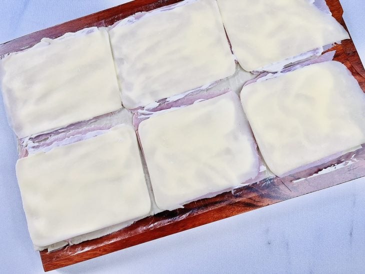 Fatias de queijo acomodadas sobre a camada de requeijão cremoso.