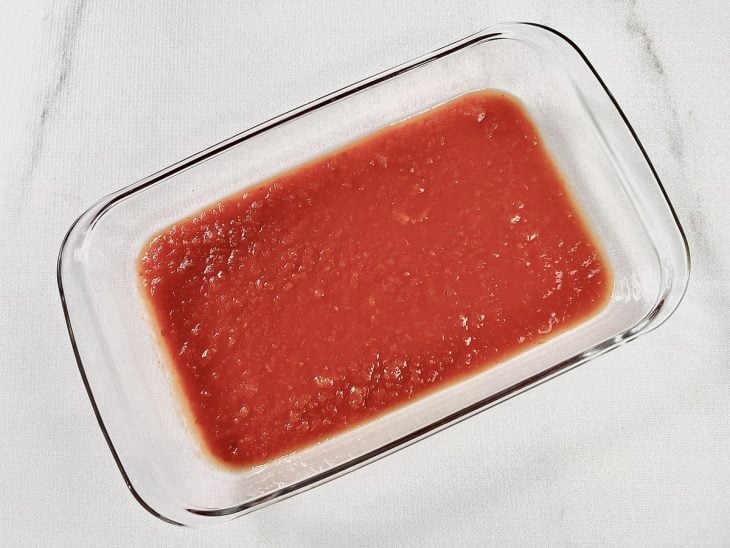 Refratário retangular com uma camada de passata rústica de tomate no fundo.