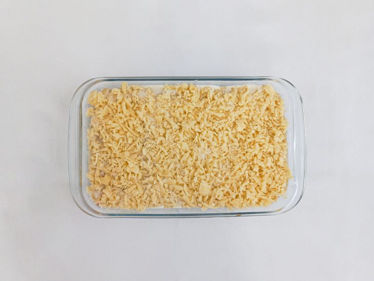 Refratário com uma camada de molho branco, canelones e queijo na superfície.