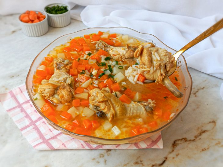 Canja de galinha com arroz cozido pronta para consumo em um recipiente grande de vidro.