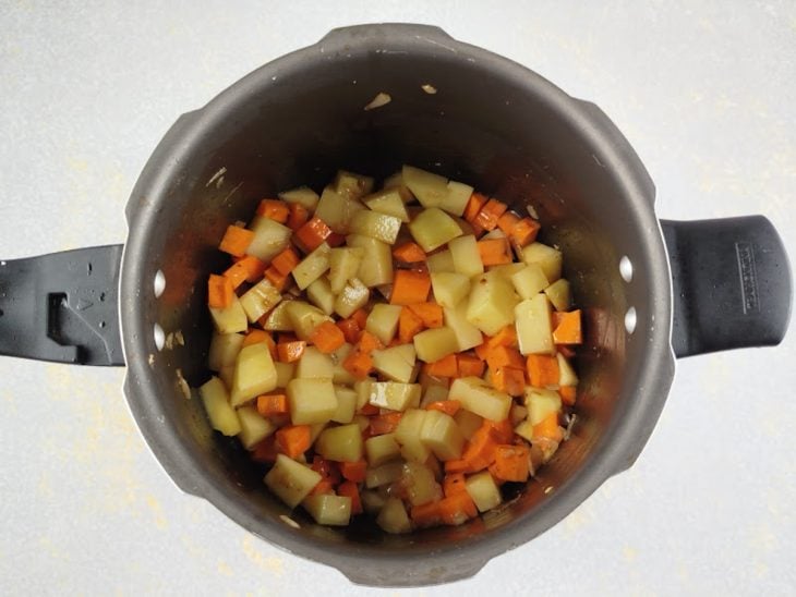 Batatas e cenouras refogando junto do alho na panela.