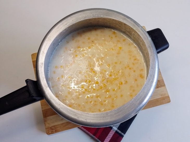 Uma panela de pressão contendo canjica, açúcar, leite, leite condensado, leite de coco e coco ralado.