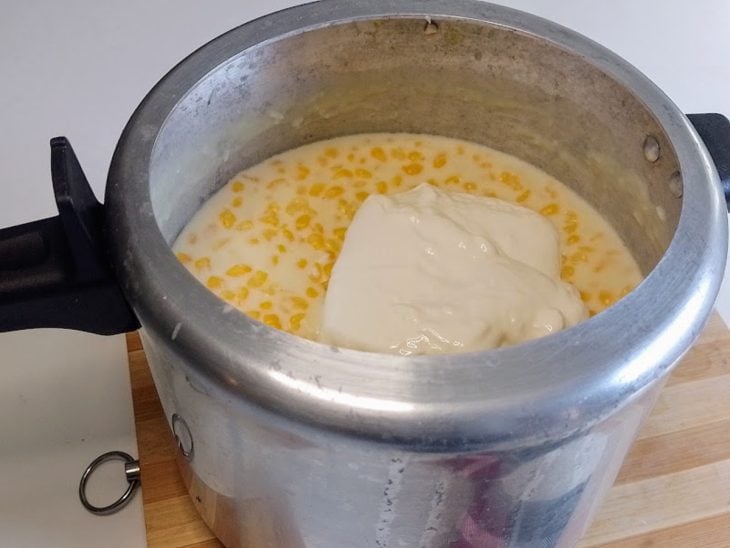 Uma panela de pressão contendo canjica, açúcar, leite, leite condensado, leite de coco, coco ralado e creme de leite.