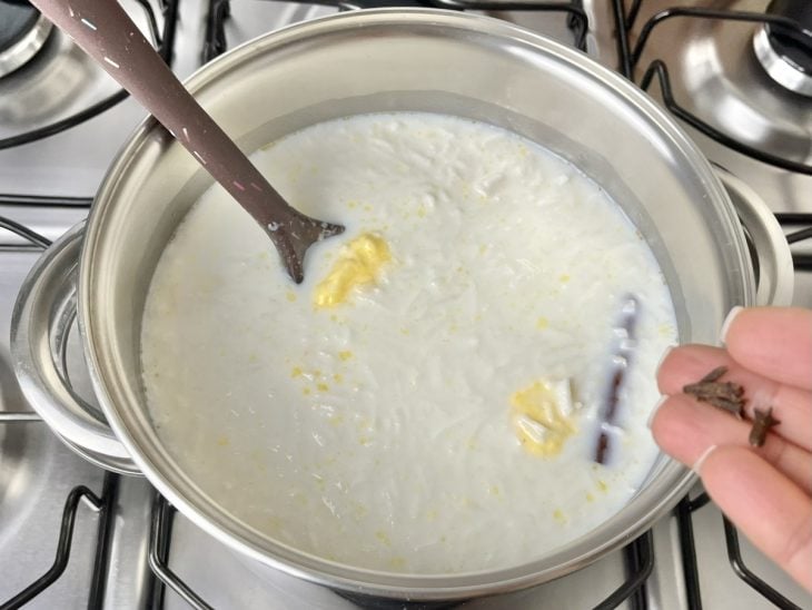 Uma panela com canjica, água, açúcar, leite, manteiga, canela, cravos, coco ralado.