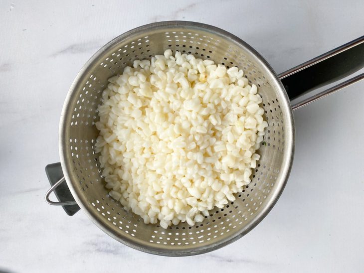 Uma peneira com canjica sobre uma panela.