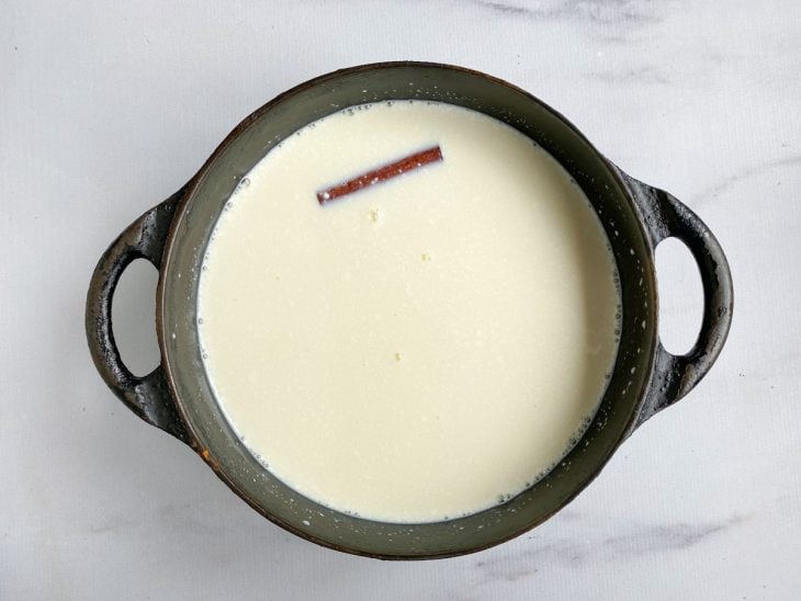 Uma panela com canjica, creme de leite, leite condensado, leite, canela e sal.