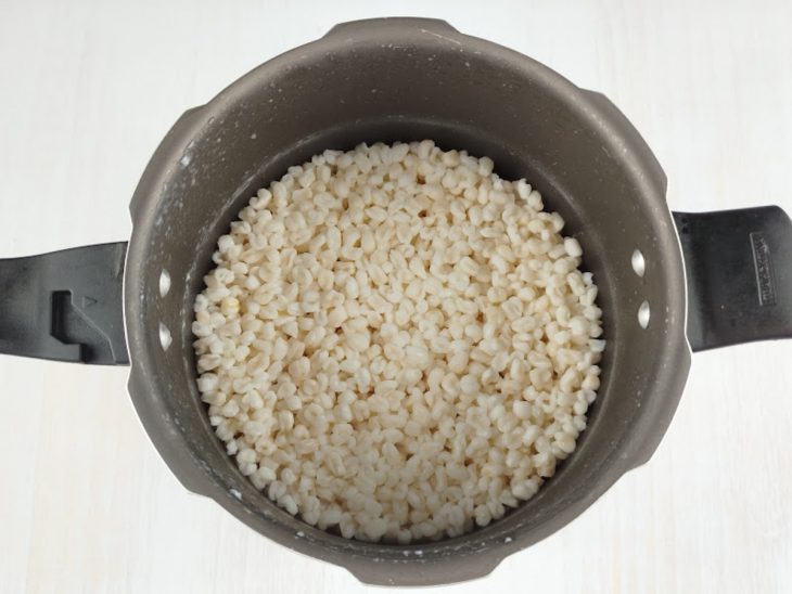 Canjica e água sendo colocadas na panela de pressão para cozimento.