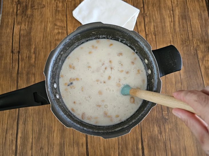 Uma panela de pressão com canjica cozido, com leite, leite de coco, leite condensado, coco ralado, açúcar e amendoim.