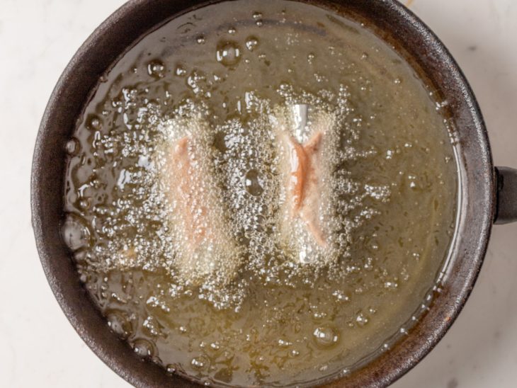 Uma frigideira com óleo quente e cannoli a fritar.
