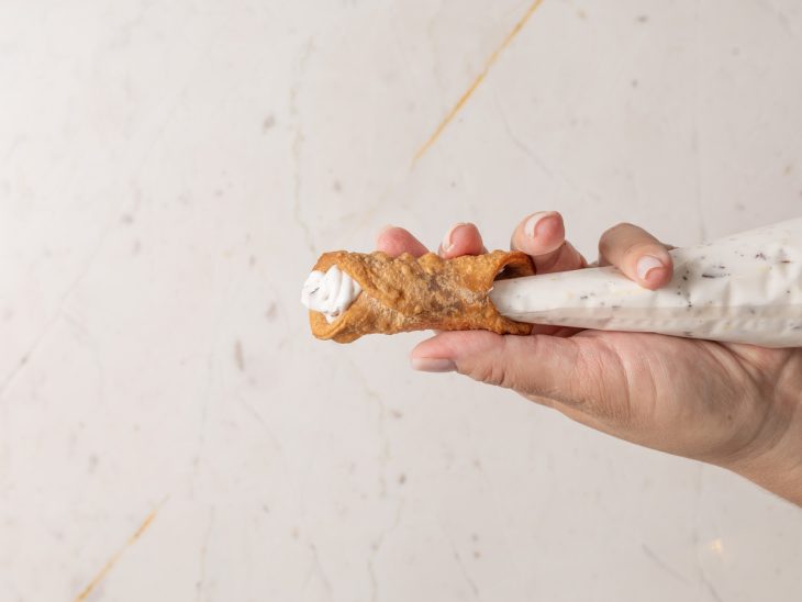 Cannoli frito sendo recheado.