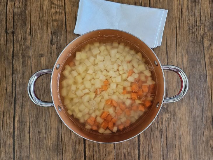 Uma panela contendi batata e cenouras picadas cobertas com água.
