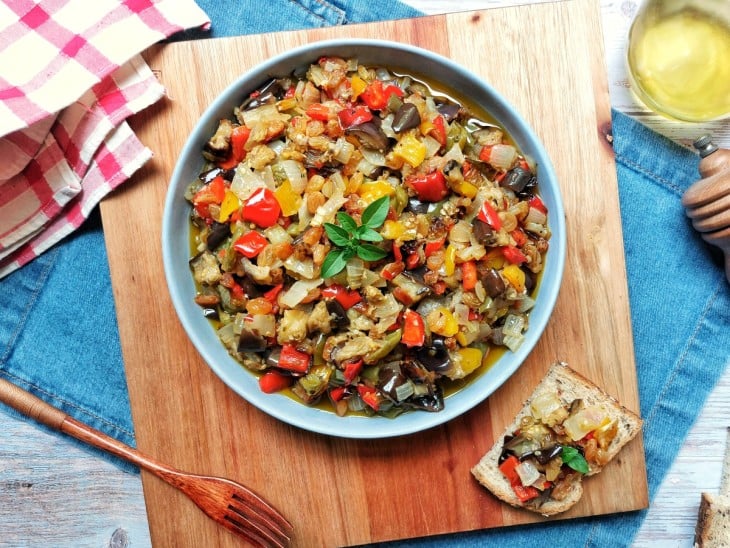 Caponata de berinjela servida em uma cumbuca com torrada ao lado com uma porção.