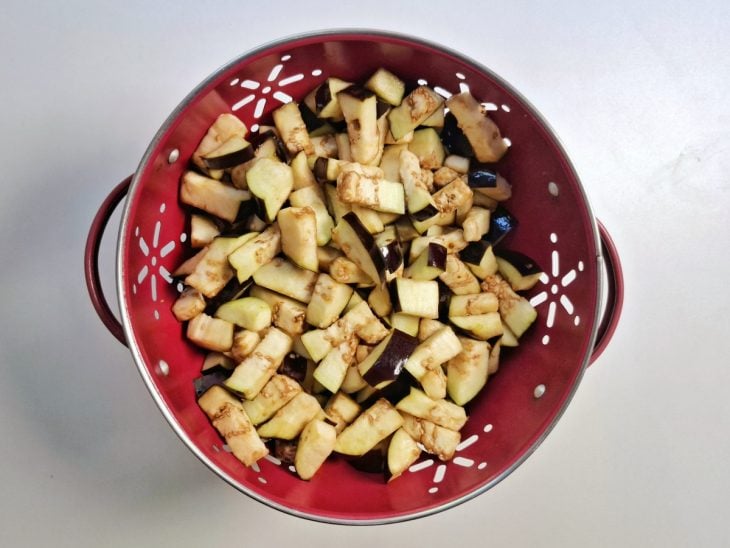 Pedaços de berinjela com sal no escorredor de macarrão.