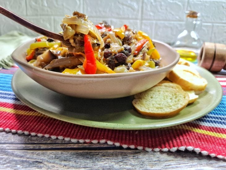 Caponata de berinjela na panela finalizada com uva-passa e servida com torradas.