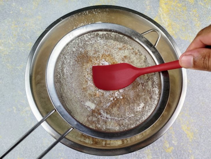 Ingredientes secos sendo peneirados e empurrados com a colher.