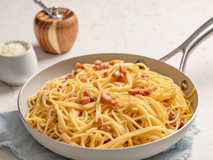 Carbonara finalizada com pimenta-do-reino pronta para consumo em uma panela branca.