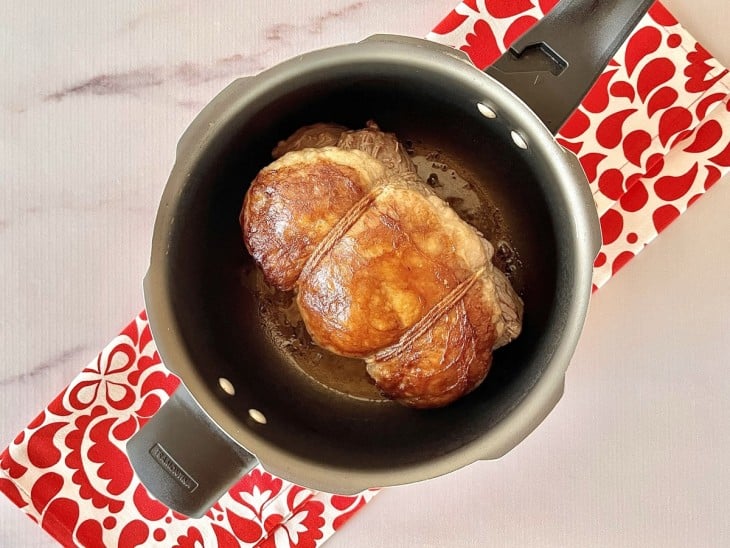 Panela de pressão com carne dourada amarrada com barbante.