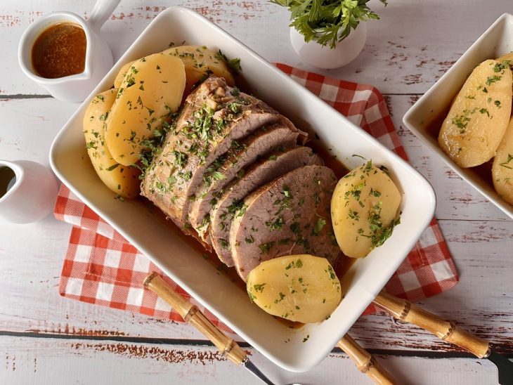 Travessa com carne assada na panela de pressão acompanhada de batatas e molho.