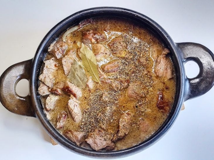 Uma panela contendo carnes e cebolas refogadas, suco e laranja, caldo aromático e temperos.