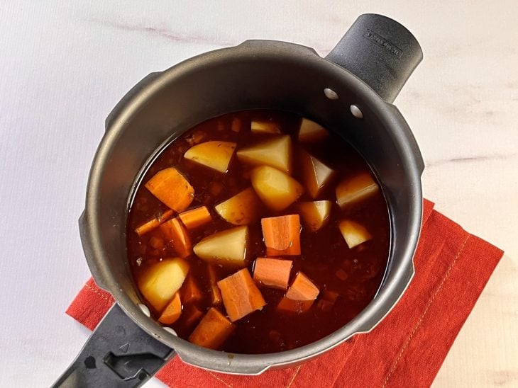 Uma panela de pressão contendo caldo e batatas cortadas.