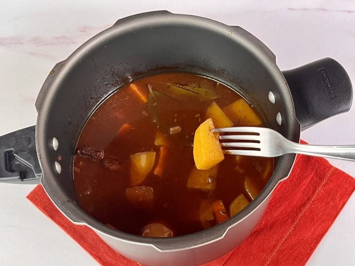 Uma panela de pressão contendo caldo e batatas cortadas.