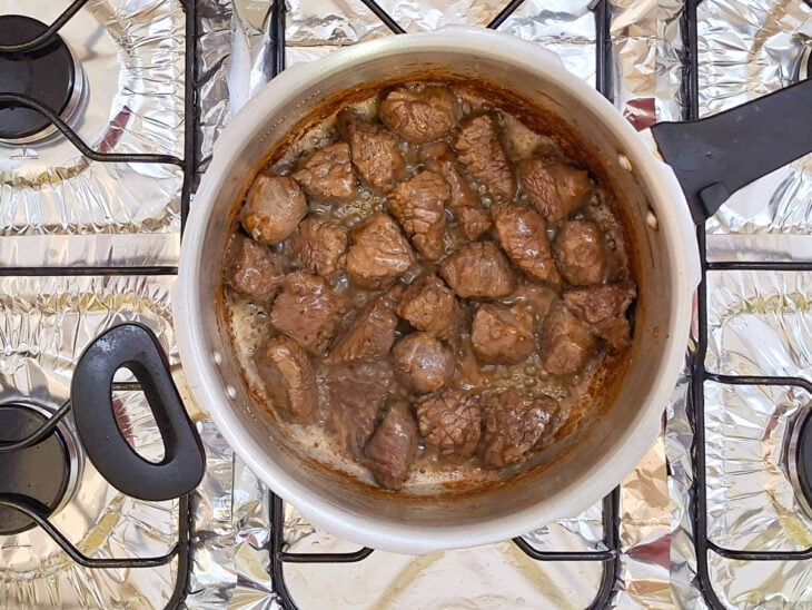 Cubos de carne bovina sendo grelhados e dourados no azeite quente no fundo da panela de pressão.